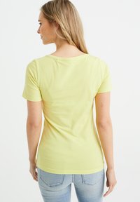 T-shirt giallo chiaro a maniche corte con collo rotondo. Materiale di cotone morbido e liscio con una forma aderente e una leggera elasticità.