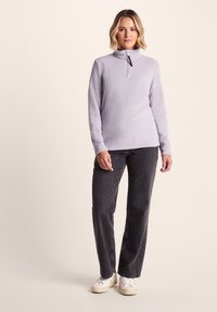 Light purple fleece quarter-zip top with a stand collar, long sleeves, and a black accent zipper, paired with dark gray straight-leg jeans and sneakers.