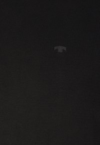 Vêtement en tricot noir avec une surface texturée et un logo discret. Le matériau semble doux et extensible, adapté pour un port décontracté.