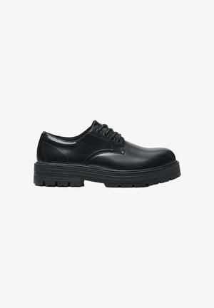Zwarte leren veterschoen met dikke geribbelde zool en afgeronde neus, zijaanzicht op witte achtergrond.