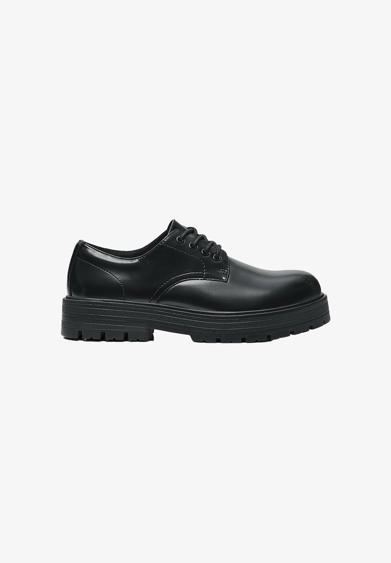 Chaussure en cuir noir à lacets avec une semelle épaisse rainurée et un bout arrondi, vue de profil sur fond blanc.