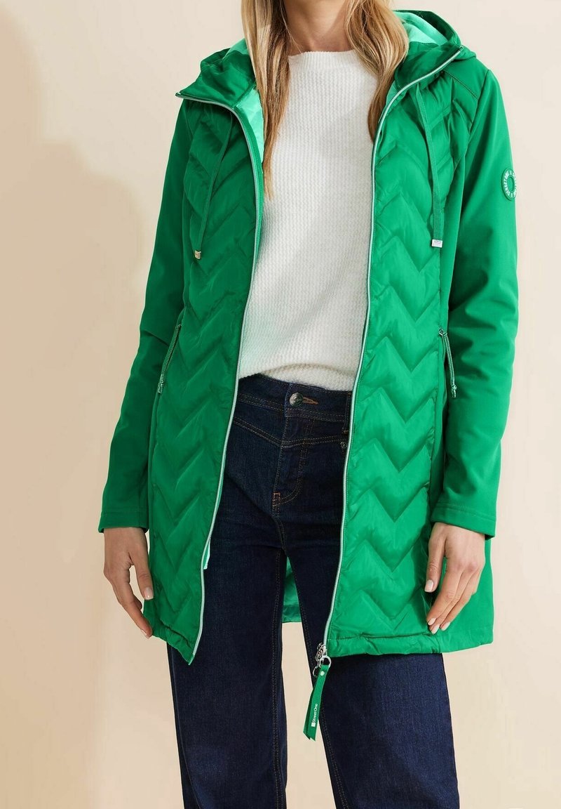 Groene pufferjas met een visgraatpatroon, capuchon en zakken met rits. Heeft een contrasterende voering en ritstrekjes als accenten.