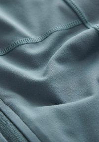 Strukturert, dæmpet blå stof med synlige syninger og en glat overflade, der viser bløde tekstilkonturer og folder.