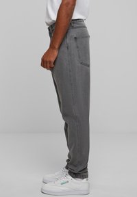 Sive traperice opuštenog kroja, s bočnim i stražnjim džepovima, stilizirane s bijelim tenisicama. Tkanina je blago teksturirana.