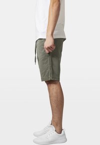 Shorts vert olive avec cordon de serrage, en tissu texturé. Portés avec un t-shirt blanc simple et des baskets blanches.