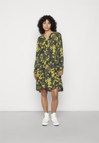 Vestido floral em azul-marinho com padrões amarelos, apresentando decote em V e mangas longas. Combinado com ténis brancos.