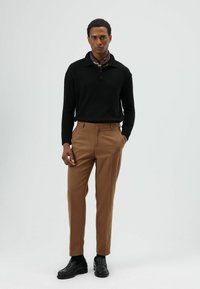 Zwarte gebreide pullover met kraag, bruine maatbroek en zwarte loafers. Outfit met een bruine en patroonrijke sjaal.