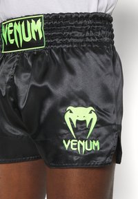 Calções de boxe de cetim pretos com um logótipo bordado verde "VENUM" e um gráfico de víbora, com um cós elástico e fendas laterais.
