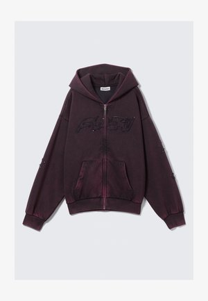 Temno vijolična zip-up kapuca z velikimi sprednjimi žepi, kapuco in izvezenim besedilom čez prsi in rokave.