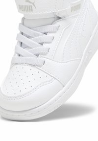Weißer Sneaker mit durchlöchtem Zehenbereich, glattem Kunstleder, hexagonalen Logo-Akzenten und flachen grauen Schnürsenkeln. Mid-Top-Design mit gepolstertem Schaft.