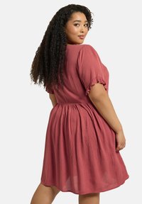 Vaaleanpunainen, teksturoitu mekko, jossa on lyhyet, röyhelömäiset hihat ja joustava vyötärö. Mekko ulottuu säären puoliväliin ja siinä on levenevä hame.