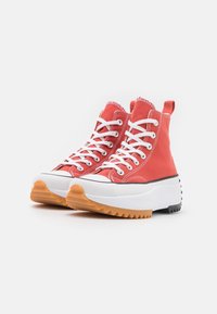 Rote High-Top-Sneaker aus Canvas mit weißen Schnürsenkeln, weißer Kappe und einer dicken Sohle mit einem orange-schwarzen Profildesign.