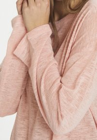 Różowy sweter dziany o luźnym kroju, szerokim dekolcie w łódkę i długich rękawach. Materiał wydaje się miękki i lekki, z teksturowanym wzorem.