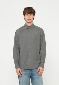 Fekete-fehér kockás hosszú ujjú ing, galléros nyakkal, gombos elejjel és bal oldali mellzsebbel. Világoskék farmerral viselve.