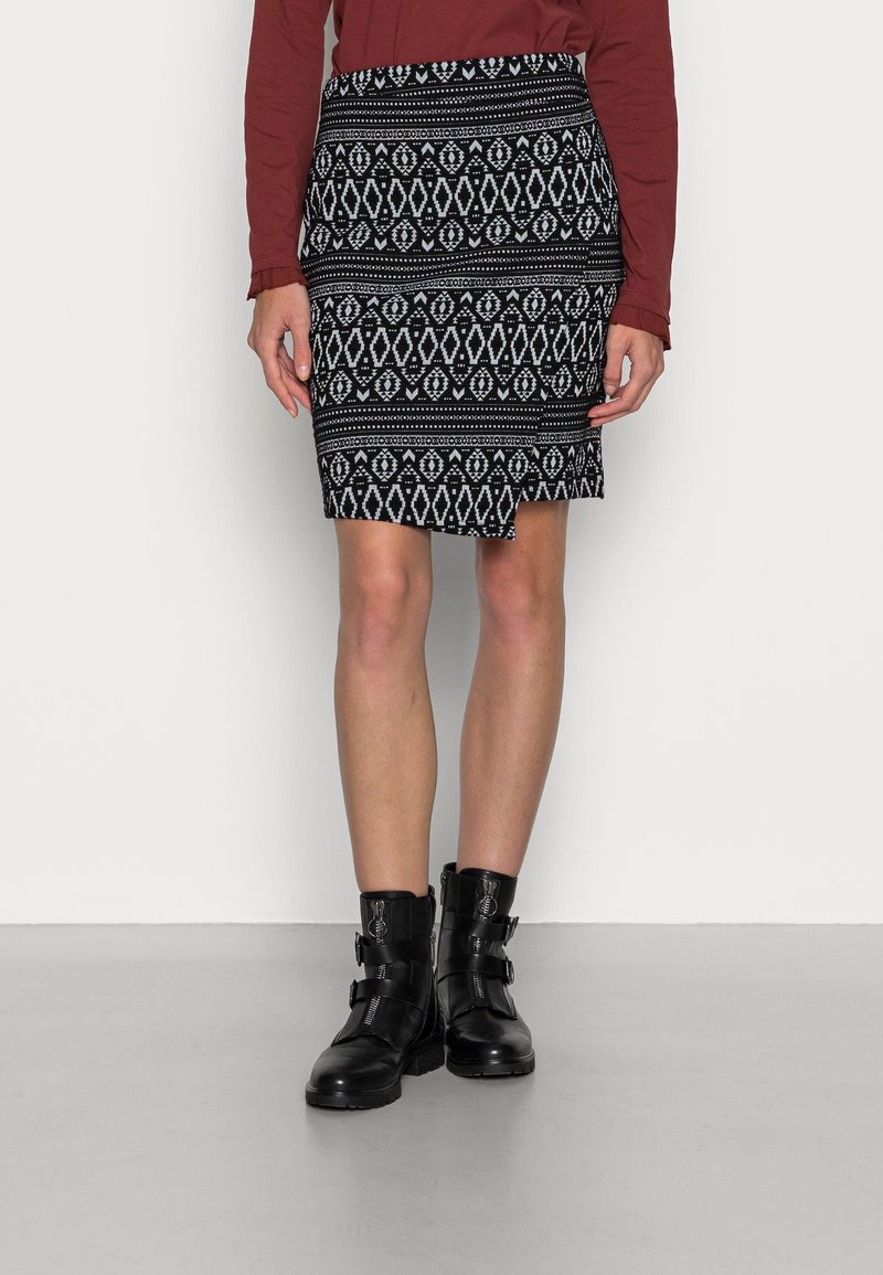 Jupe mi-longue à motifs géométriques noir et blanc portée avec un haut rouge à manches longues et des bottines noires à boucle.