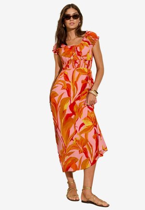 Robe longue à motifs floraux vifs en rose, orange et jaune. Manches volantées, taille smockée et design fluide. À assortir avec des sandales dorées.