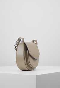Beżowa torebka typu crossbody o fakturowanej powierzchni, zaokrąglonym kształcie, klapce składanej oraz srebrnym wykończeniu z łańcuszka.