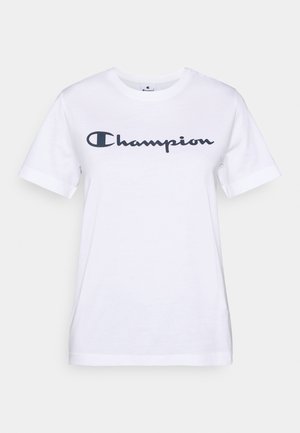T-shirt en coton blanc à manches courtes et col rond, arborant un logo "Champion" bleu marine sur la poitrine. Texture douce, design basique.