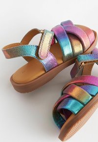 Sandales pour enfants avec semelles marron et brides arc-en-ciel scintillantes munies de fermetures velcro, présentées sur un fond blanc.