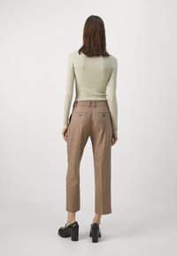 Maglione a coste di colore verde chiaro abbinato a pantaloni a vita alta con fantasia a quadri marroni. Scarpe con tacco chunky nere completano l'outfit.