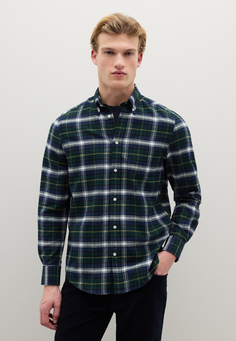 Camicia di flanella verde e blu navy con motivo a quadri di linee bianche e gialle, colletto con bottoni e maniche lunghe.