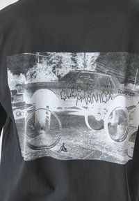 Schwarzes T-Shirt mit einem großen grafischen Druck eines Autos mit Fahrrädern in Graustufen. Das Material besteht aus weicher Baumwolle und eignet sich für legere Kleidung.