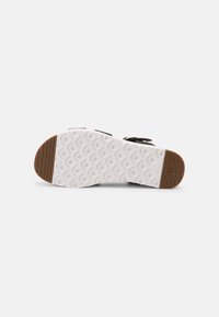 Semelle de sandale avec motif texturé blanc et sections en caoutchouc marron au talon et à l'orteil, montrant le design antidérapant et le logo de la marque au talon.