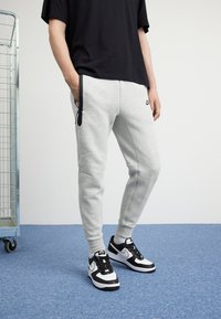 Pantaloni grigi in felpa con un design affusolato e dettagli neri, abbinati a sneakers bianco e nere. Tessuto morbido e tasche laterali incluse.