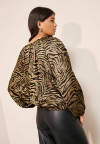 Schwarze und goldene Zebra-Print-Bluse mit lockerer Passform, gerafftem Halsausschnitt und langen Puffärmeln, kombiniert mit hochtaillierten schwarzen Hosen.