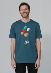 T-shirt en coton teal avec un astronaute tenant des ballons-planètes colorés. Le design comprend des textures et des nuances variées représentant les planètes.