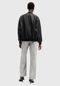 Chaqueta bomber de cuero negra con puños y bajo acanalados, combinada con pantalones de mezclilla anchos desgatados en gris claro y tacones negros puntiagudos.