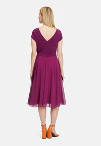 Lila ärmelloses Kleid mit V-Ausschnitt, tailliertem Bund und schwingendem Rock. Kombiniert mit orangefarbenen Blockabsatzsandalen.