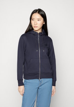 Marinefarbener Reißverschluss-Hoodie aus weichem Material, mit einer Kapuze mit Kordelzug, Fronttaschen und gerippten Bündchen sowie Saum. Dezentes Logo auf der Brust.