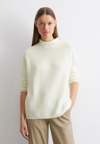 Crème kleurige sweater met hoge hals, lange mouwen, zachte textuur en een ontspannen pasvorm. Gecombineerd met lichtbeige broeken met een minimalistisch design.