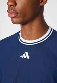 Jūrinė sportinė marškinė su apvaliu iškirpimu, su balta dryžuota apykakle ir baltu logotipu ant krūtinės. Lygus, lengvas audinys.