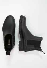 Bottes de cheville noires en caoutchouc avec panneaux élastiques sur les côtés et languette de tirage. Fini lisse et mat avec une semelle en caoutchouc texturée pour une meilleure adhérence.