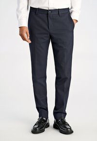 Marineblaue Anzughose in einem schlanken, maßgeschneiderten Design mit flacher Vorderseite und Bügeldetails; kombiniert mit schwarzen Lederschuhen und einem weißen Hemd.