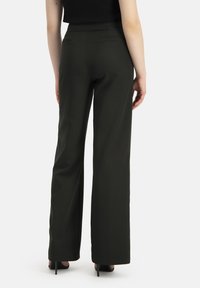 Donkergroene wijde broek gemaakt van gladde stof, met twee achterzakken en een getailleerde pasvorm. Gestyled met zwarte hoge hakken.