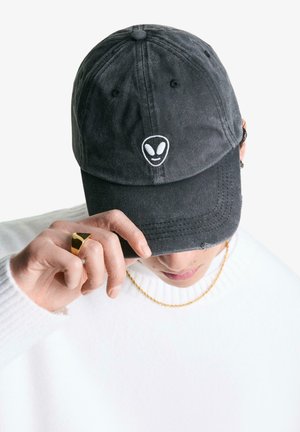 Zwarte baseballpet van katoen met een alien gezicht logo in het wit geborduurd op de voorkant. Heeft een gebogen rand en een verstelbare band.