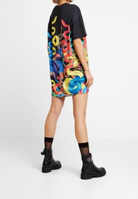 Oversized black t-shirt featuring a vibrant snake pattern in multiple colors. Model wears black ankle boots with a buckle detail and sheer socks.