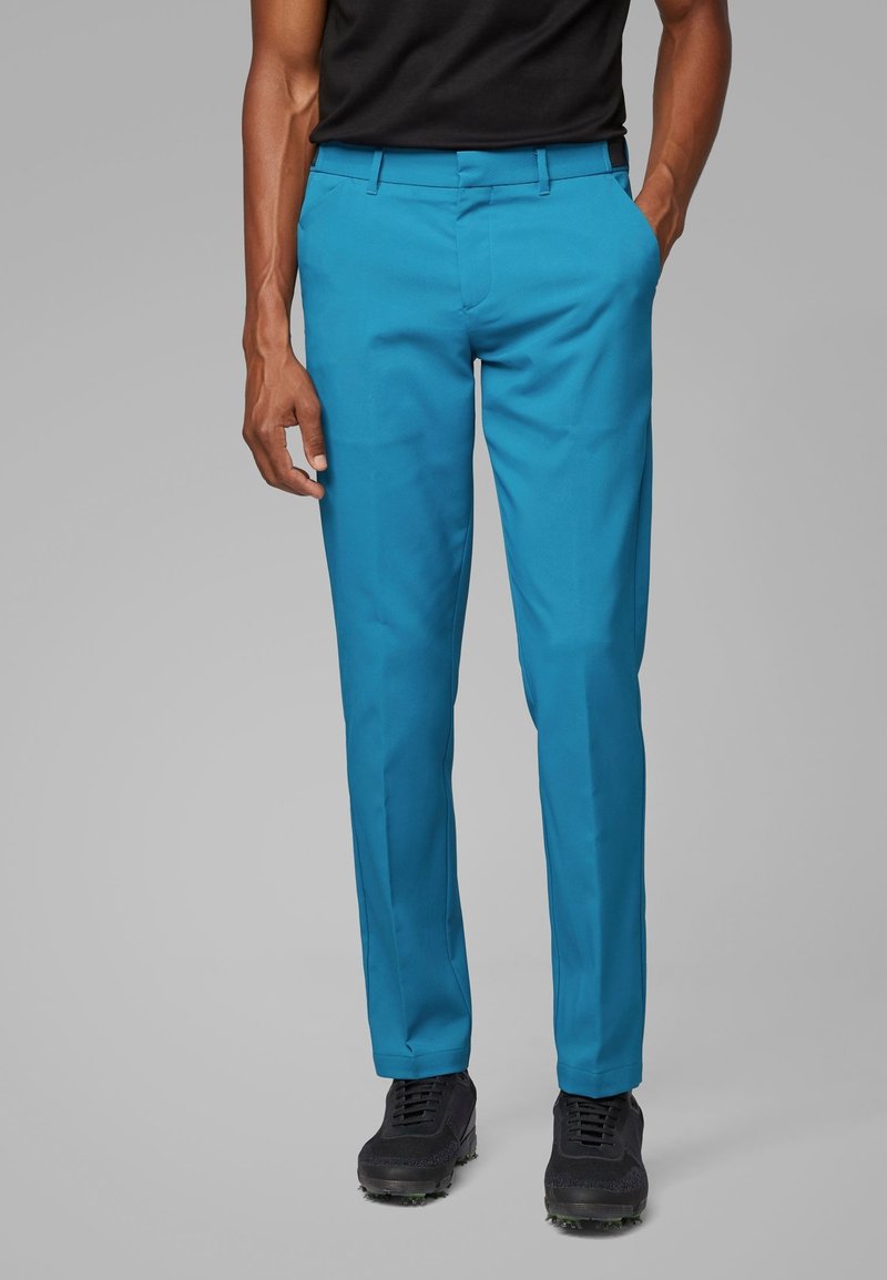 Tyrkysové kalhoty z lehké látky, s úzkým střihem, hladkým předním dílem a bočními kapsami, doplněné černými botami.