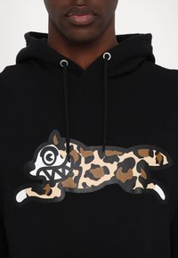 Housse noire avec un grand graphisme ludique d'un chat dans un motif léopard beige et marron, avec des accents blancs pour les yeux et les dents.