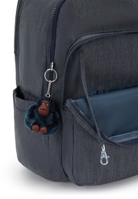 Ryggsäck i mörk denim med silverdragkedja. Har en fluffig apa nyckelring fäst, mörkblå färg med bruna detaljer.