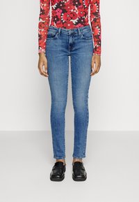 Jeans de denim azul skinny con un acabado desgastado, diseño de cinco bolsillos y un ajuste de cintura media, combinados con mocasines negros.