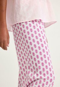 Ljust rosa linnetopp i kombination med vita byxor som har ett upprepande mönster av pinka blommor. Tyget har en texturerad yta.