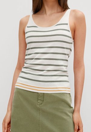 Kobieta nosząca biały top z szarymi poziomymi paskami i żółtym wykończeniem, w połączeniu z oliwkowo zieloną spódnicą.