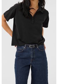 Svart kortärmad pikétröja med tre knappslå, kombinerad med högmidjade mörkblå raka jeans och ett svart bälte.