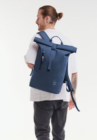 Merimies rullausreppua, joka on valmistettu kestävästä materiaalista, etutaskuvetoketjulla, säädettävillä hihnoilla ja hillityllä logotunnuksella.