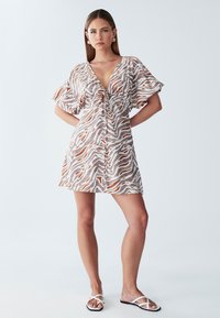 Abito a maniche corte con scollo a V, dettaglio con cordoncino e tessuto beige con motivi astratti marroni e arancioni.