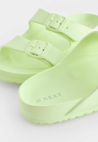 Sandales vertes en matériau doux et texturé avec deux boucles réglables. Présente un semelle intérieure profilée et une semelle extérieure striée pour une meilleure adhérence.